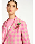 A woman wearing a pink checkered coat and a pepper-shaped brooch with glass rhinestones on a soft felt base.