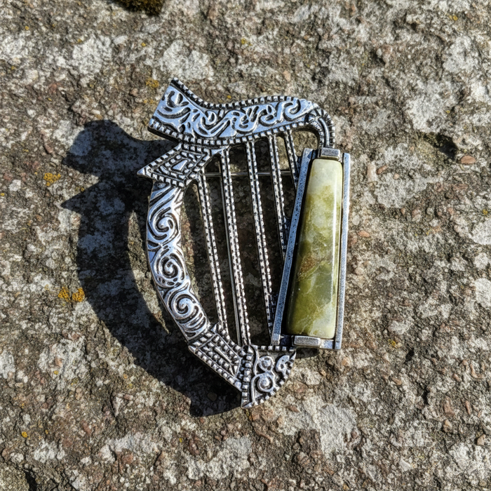 Silver harp-shaped brooch with a green stone on a textured stone surface
