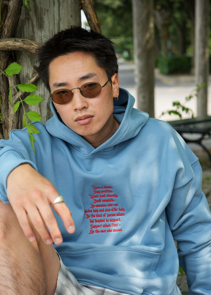 Person wearing a lightweight terry hoodie with red embroidered text outdoors, showcasing a relaxed style.