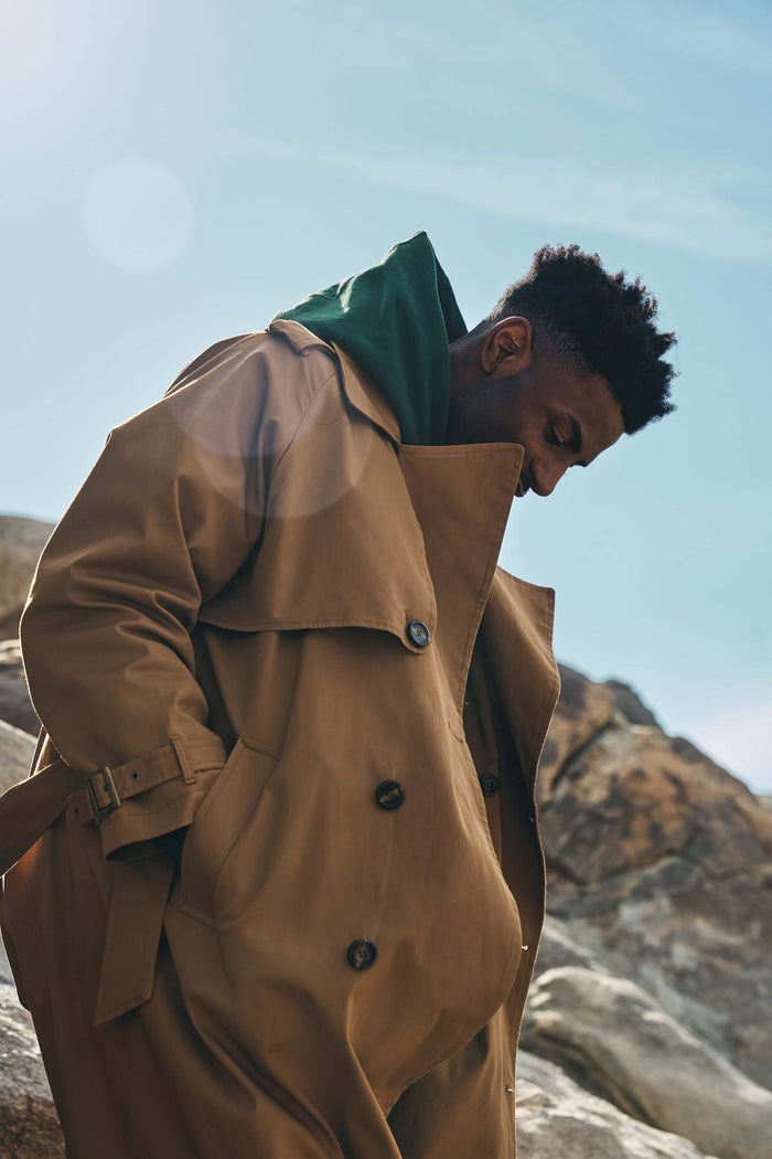 Men’s Camel Trench Coat worn by a man standing on rocks, featuring a double-breasted silhouette and belted waist.