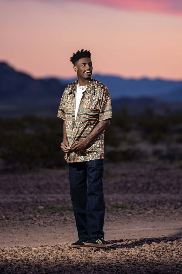 Man wearing a stylish patterned shirt and men's premium denim jeans against a scenic sunset backdrop.