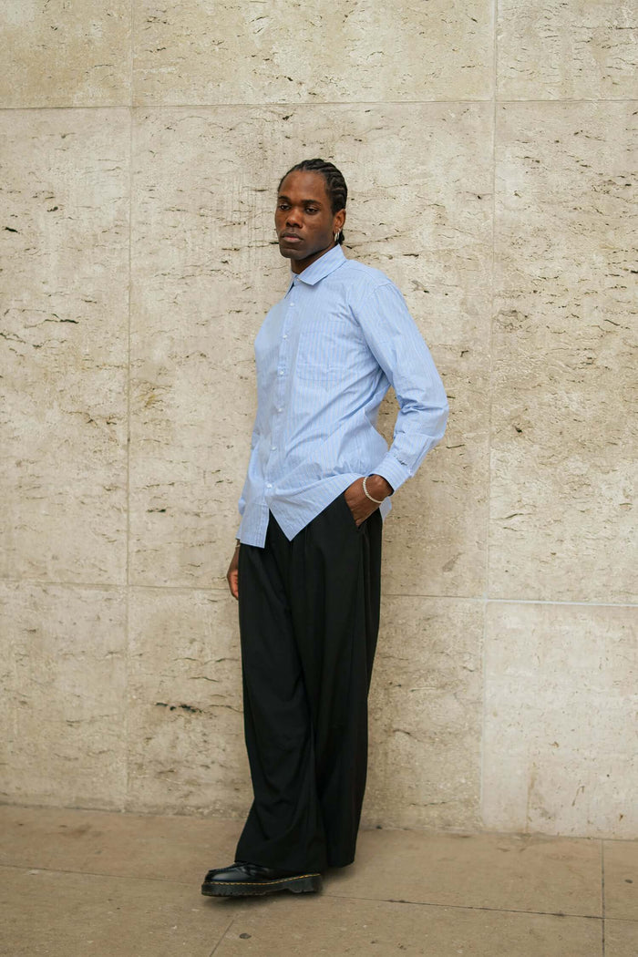 model wearing men's striped casual shirt in light blue stripes leaning against wall