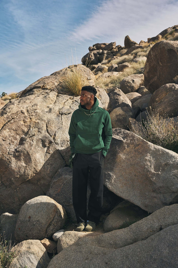 Man wearing a mid weight cotton hoodie standing on rocks in a natural setting.