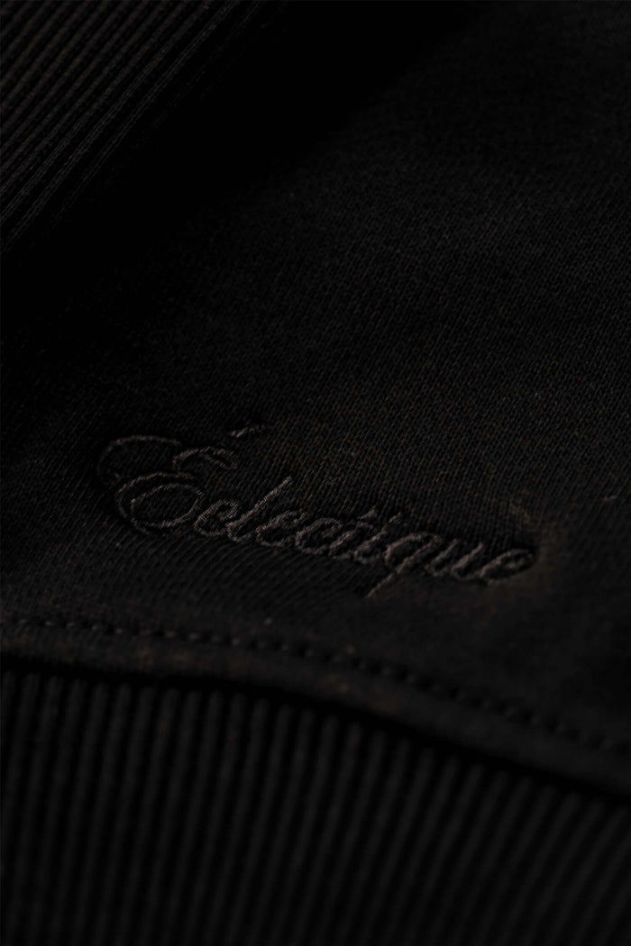 Close-up of black midweight cotton hoodie fabric featuring 'Eclectique' embroidered logo.