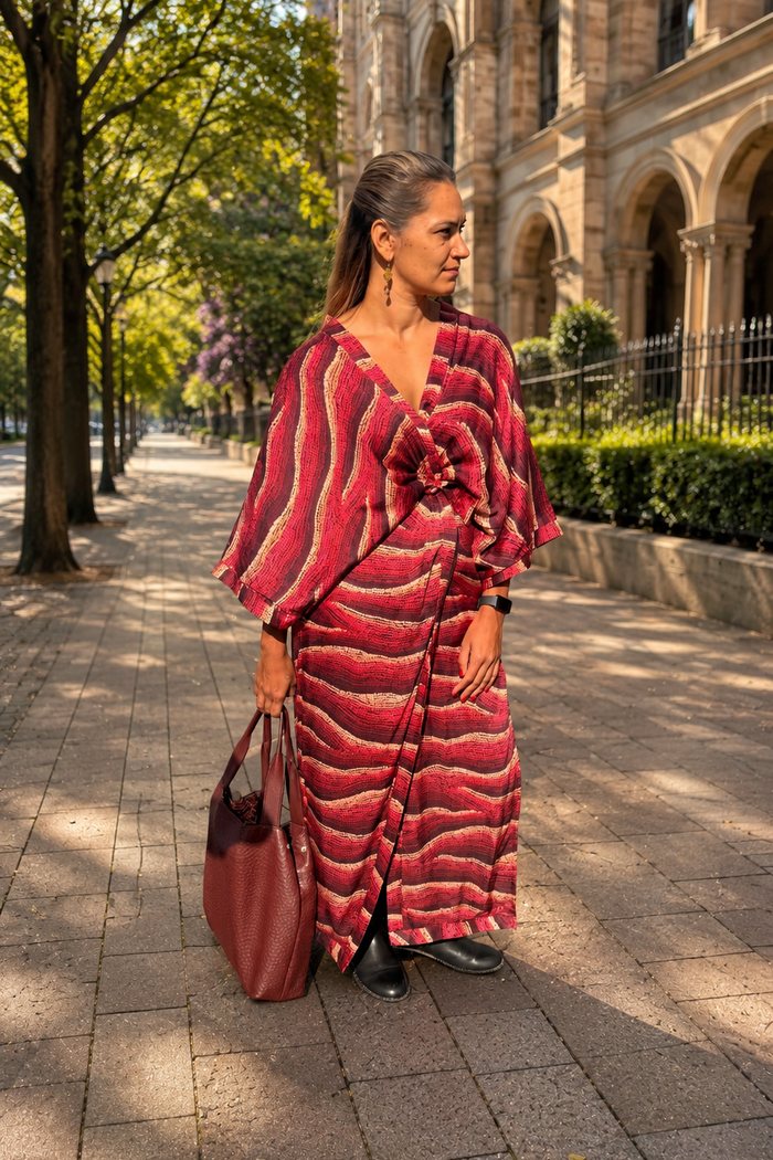Aboriginal woman in a Aboriginal patterned dress walking on a sidewalk with a building in the background