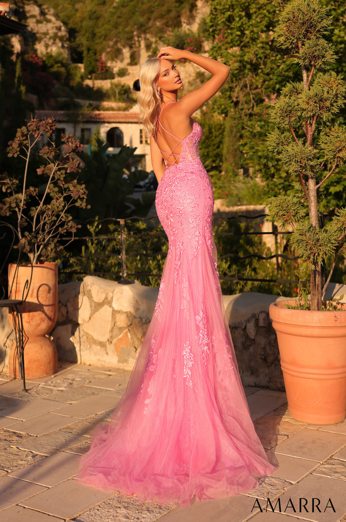 A blonde woman wears a pink lace mermaid gown with a long tulle train in a garden setting.