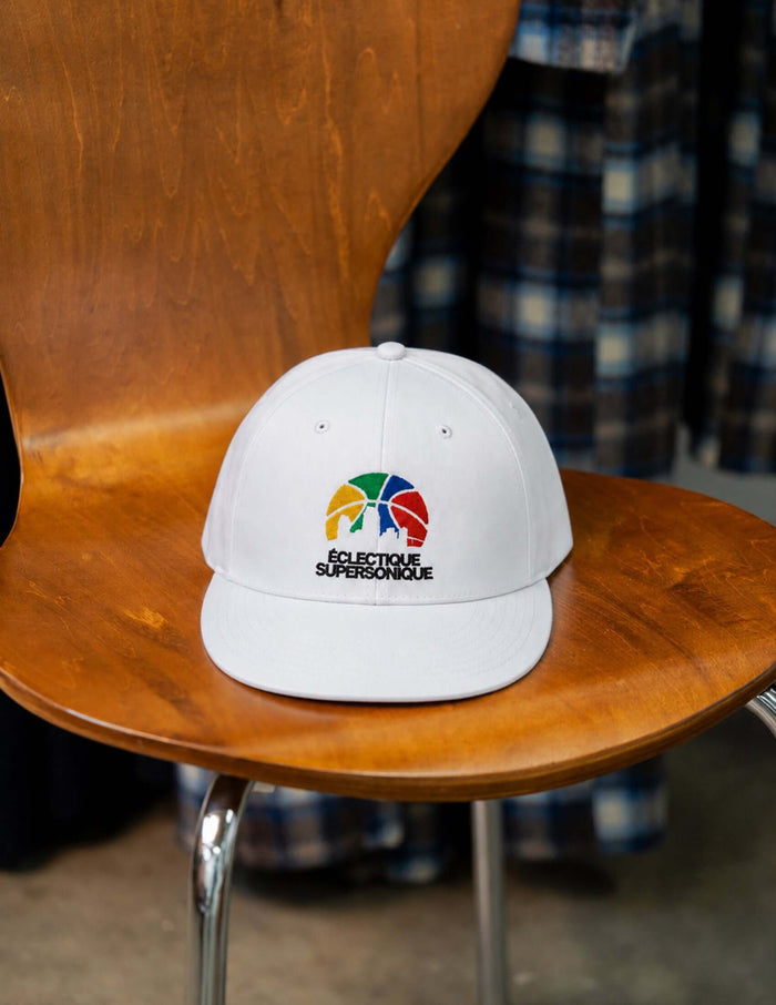 Super Sonique baseball cap displayed on a wooden chair, featuring colorful embroidery and a flat brim.