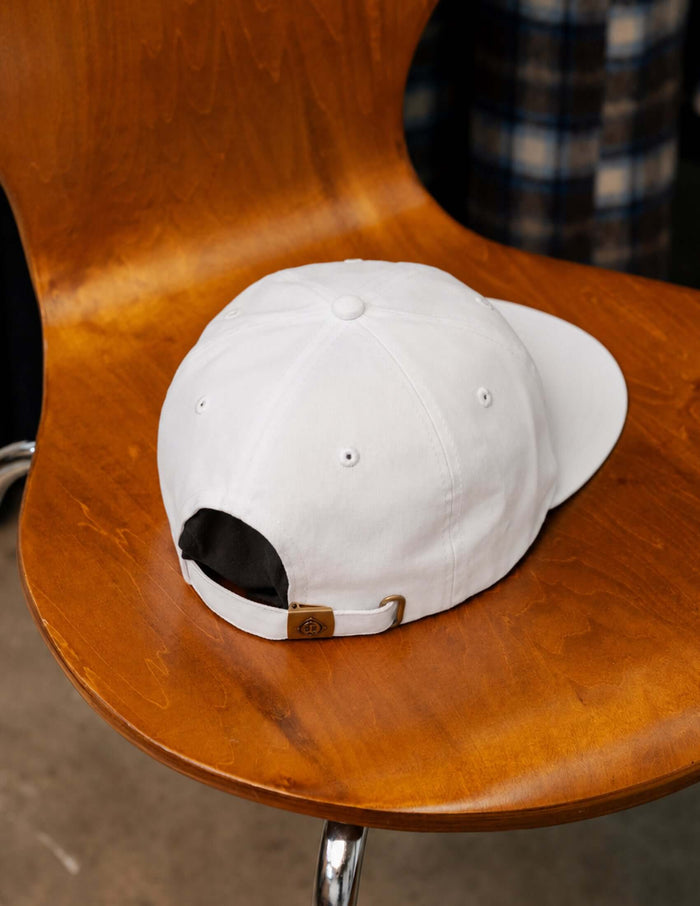 Back view of Super Sonique 5-panel baseball cap resting on a wooden chair, showcasing white cotton material and adjustable strap.